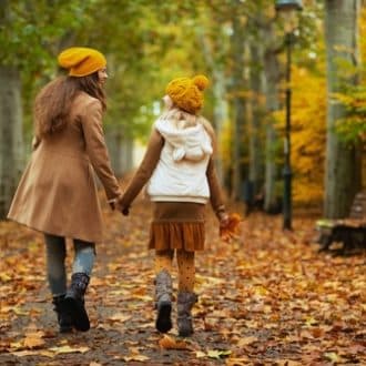 mother and child in yellow hats with autumn yellow leaves walking outside on the city park in autumn.