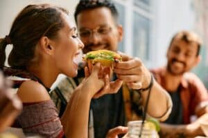 Young woman playfully eating her boyfriend’s tacos during lunch at a Mexican restaurant, concept of fun date and casual dining