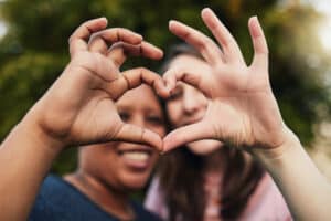Roommates smiling and making a heart hand gesture together, showing friendship, unity, and positive connection