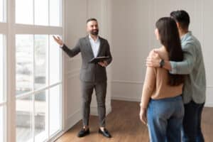 Leasing agent showing prospective renters the natural light in an unfurnished apartment during a tour.